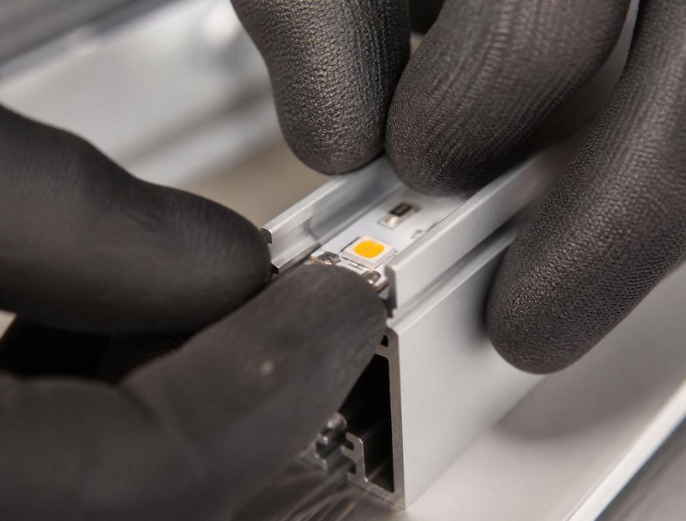 Hände in Arbeitshandschuhen setzen ein LED-Modul in ein Aluminiumprofil ein